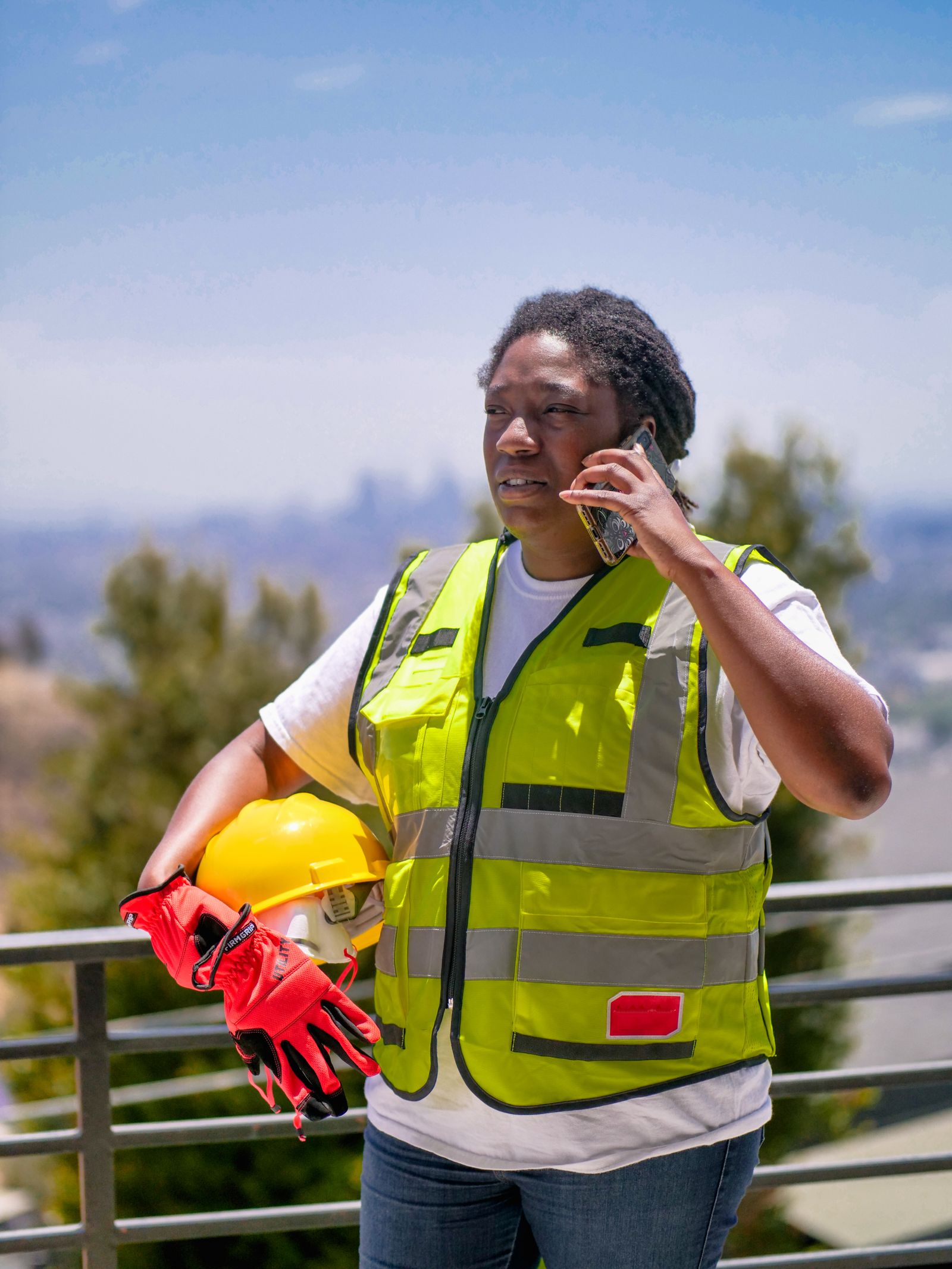 A tradesperson in high-visibility workwear on a job site, answering a phone call